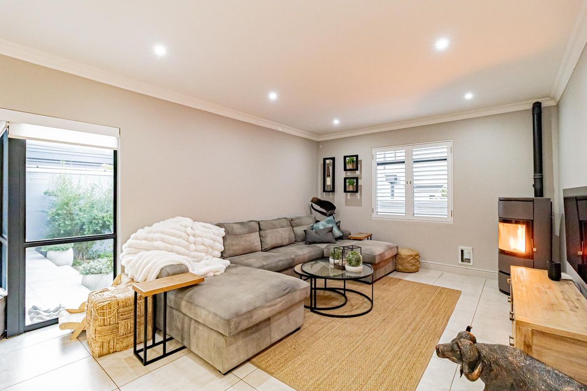 A bright and inviting living room featuring tiled flooring, recessed ceiling lighting, plantation shutters, and a modern freestanding fireplace.