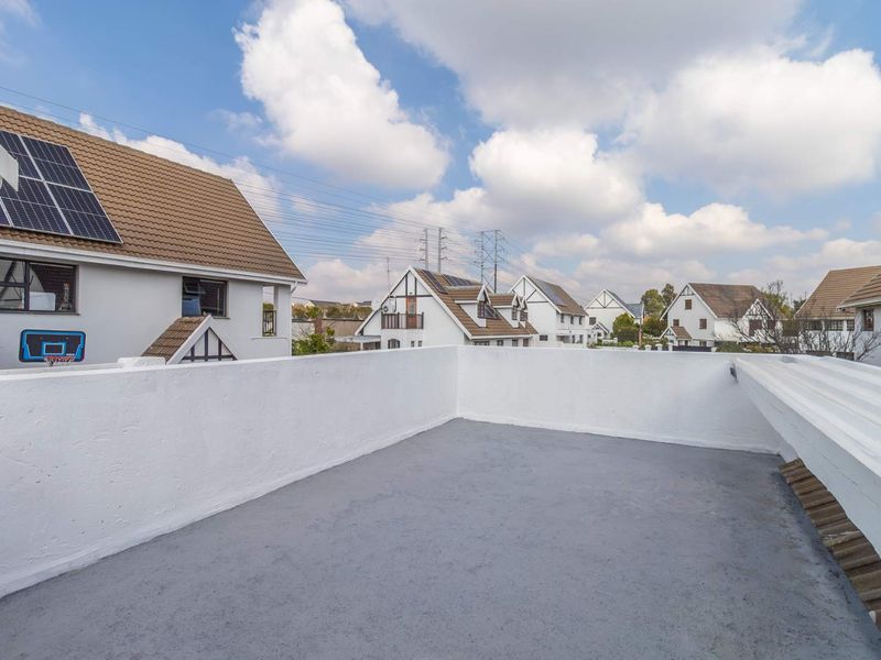 An open-air rooftop balcony featuring a painted concrete floor and white parapet walls, offering views of the surrounding residential neighborhood.