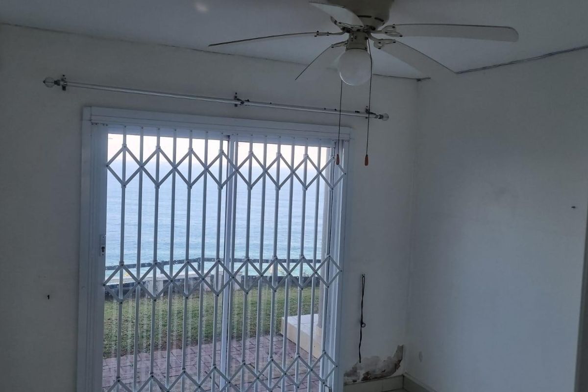 Empty bedroom featuring a ceiling fan and sliding glass door with security gate, offering direct access to an outdoor area with ocean views.