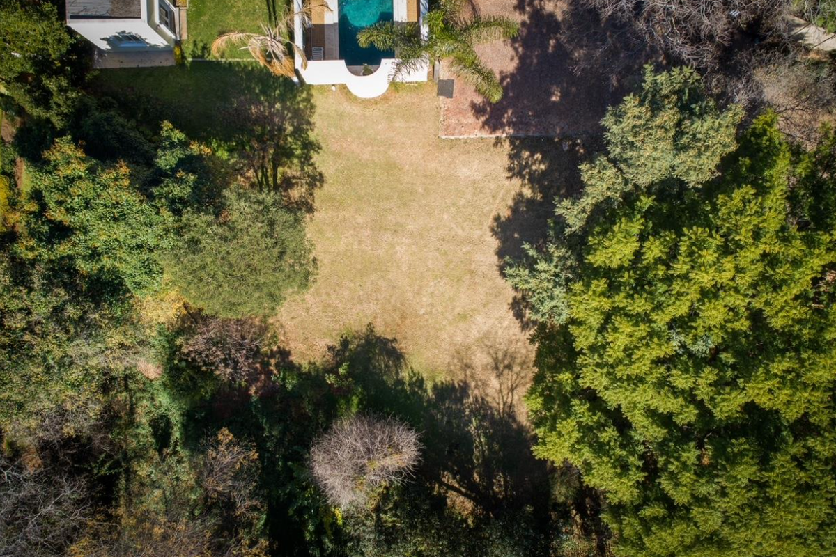 Aerial view of a residential vacant land plot featuring a swimming pool and established mature trees surrounding the perimeter.