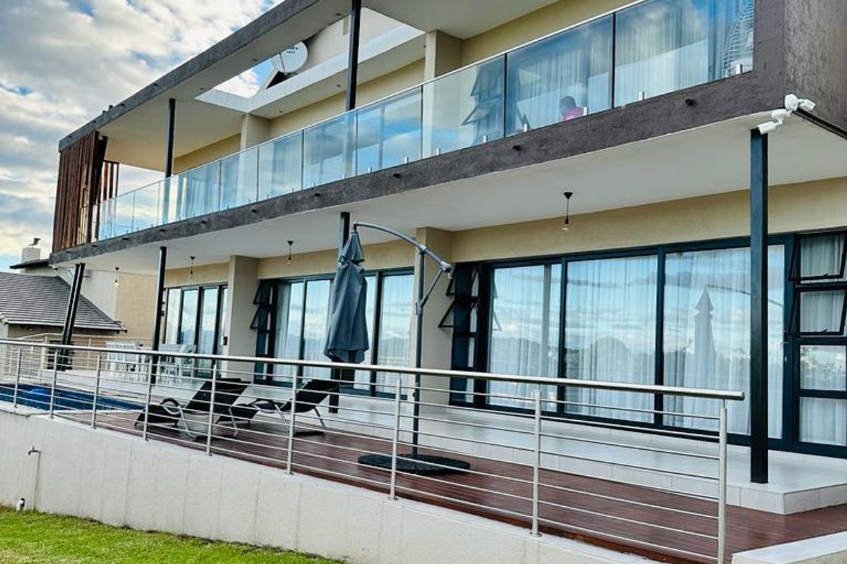 Modern multi-level exterior rear view featuring a spacious wooden deck, glass balustrades, and large sliding doors leading to the interior living spaces.