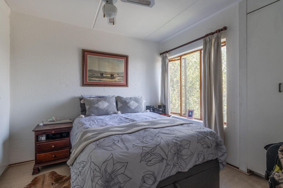 A functional bedroom featuring built-in wardrobe storage, a ceiling fan, and large windows allowing for natural light.