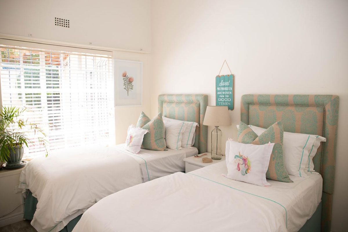 A bright bedroom featuring twin beds, neutral walls, and a large window with fitted blinds, providing natural light and a comfortable living space.