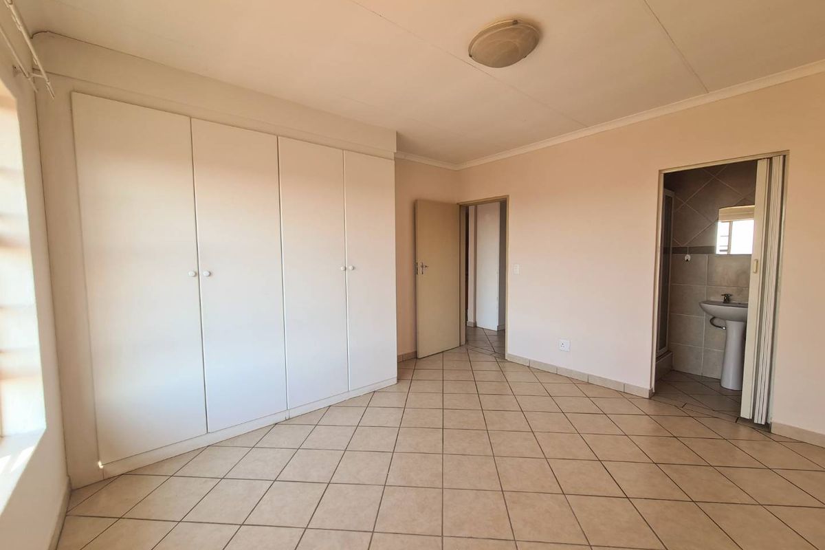 A bedroom featuring built-in cupboards, tiled flooring, and an en-suite bathroom access.