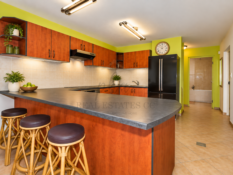 A functional kitchen featuring wood-tone cabinetry, a breakfast bar, tiled backsplash, and integrated appliances, leading to a hallway and bathroom area.