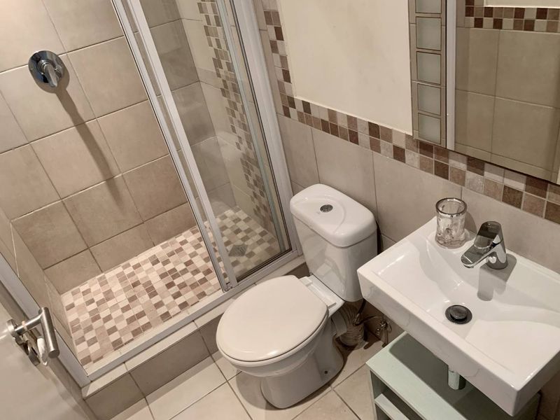 A functional bathroom featuring a shower enclosure, toilet, and wall-mounted washbasin with neutral tiled finishes and decorative mosaic accents.