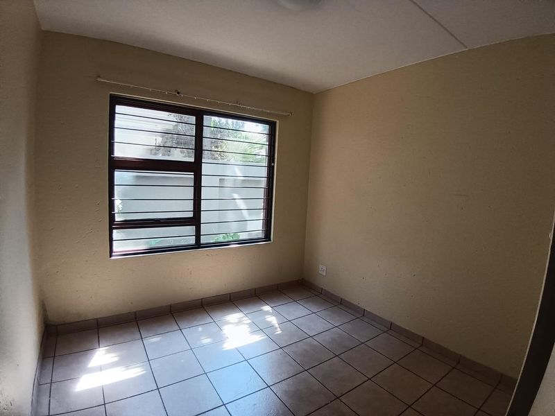 An empty bedroom featuring tiled flooring, security bars on the window, and neutral wall finishes, offering a blank canvas for potential updates.