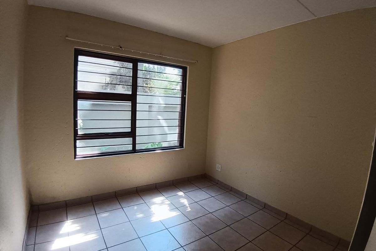 An empty bedroom featuring tiled flooring, security bars on the window, and neutral wall finishes, offering a blank canvas for potential updates.