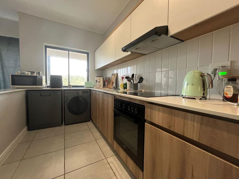 Modern kitchen featuring wood-finish cabinetry, stone countertops, tiled backsplash, and integrated appliances including an oven, hob, and extractor fan.