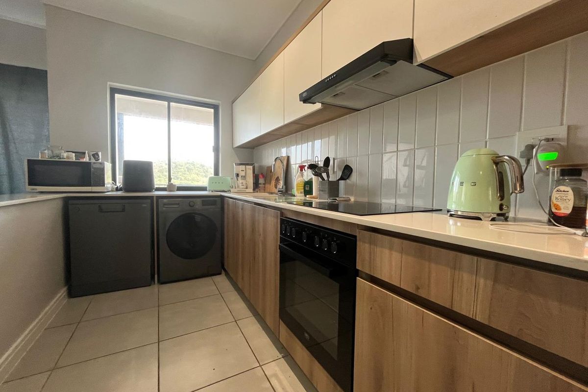 Modern kitchen featuring wood-finish cabinetry, stone countertops, tiled backsplash, and integrated appliances including an oven, hob, and extractor fan.