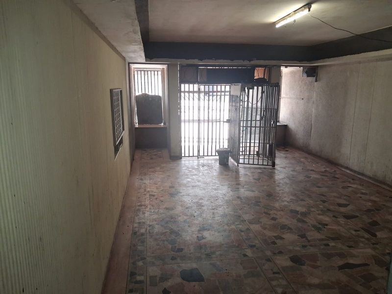 An empty, dated living area featuring terrazzo flooring, security gates, and security bars, requiring significant cosmetic refurbishment and wall repairs.