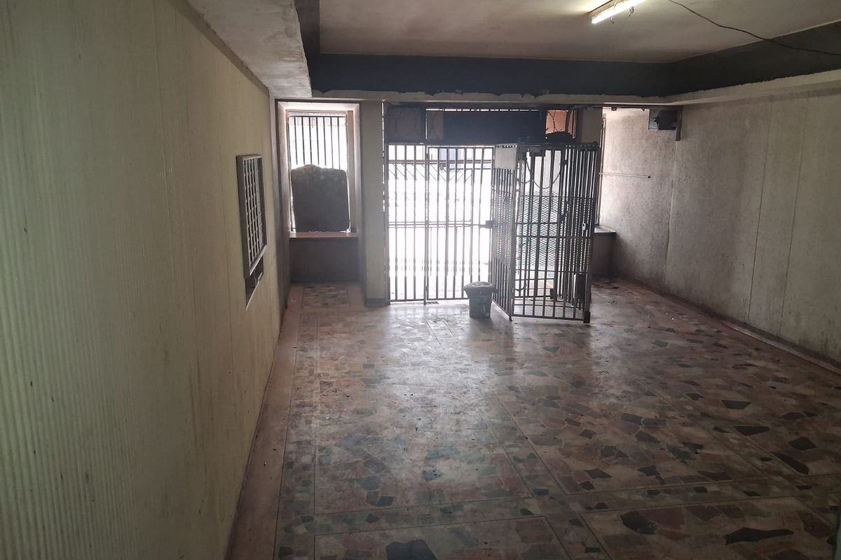 An empty, dated living area featuring terrazzo flooring, security gates, and security bars, requiring significant cosmetic refurbishment and wall repairs.