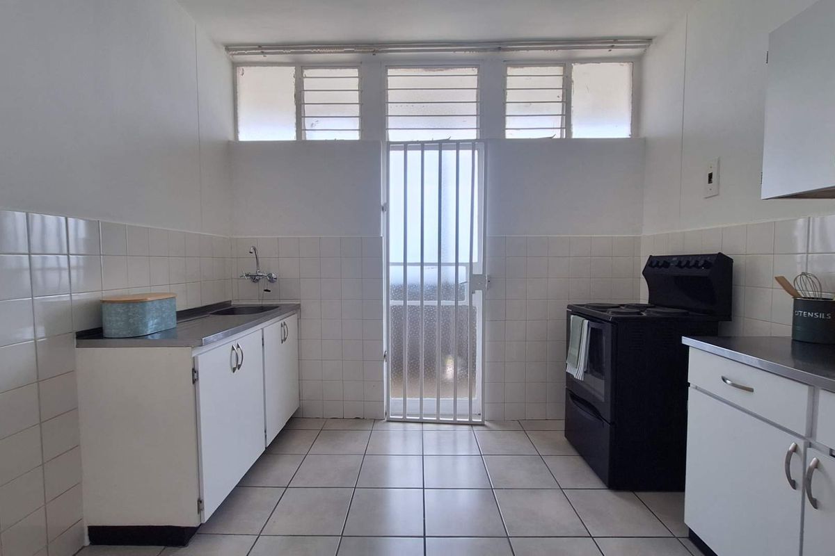 A functional kitchen featuring tiled flooring, white cabinetry, a stainless steel sink, and a security gate leading to an exterior area.