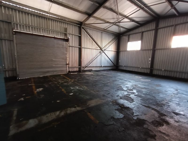 Spacious industrial warehouse or garage unit featuring high ceilings, exposed steel structural elements, and a large roller shutter door for vehicle or equipment access.