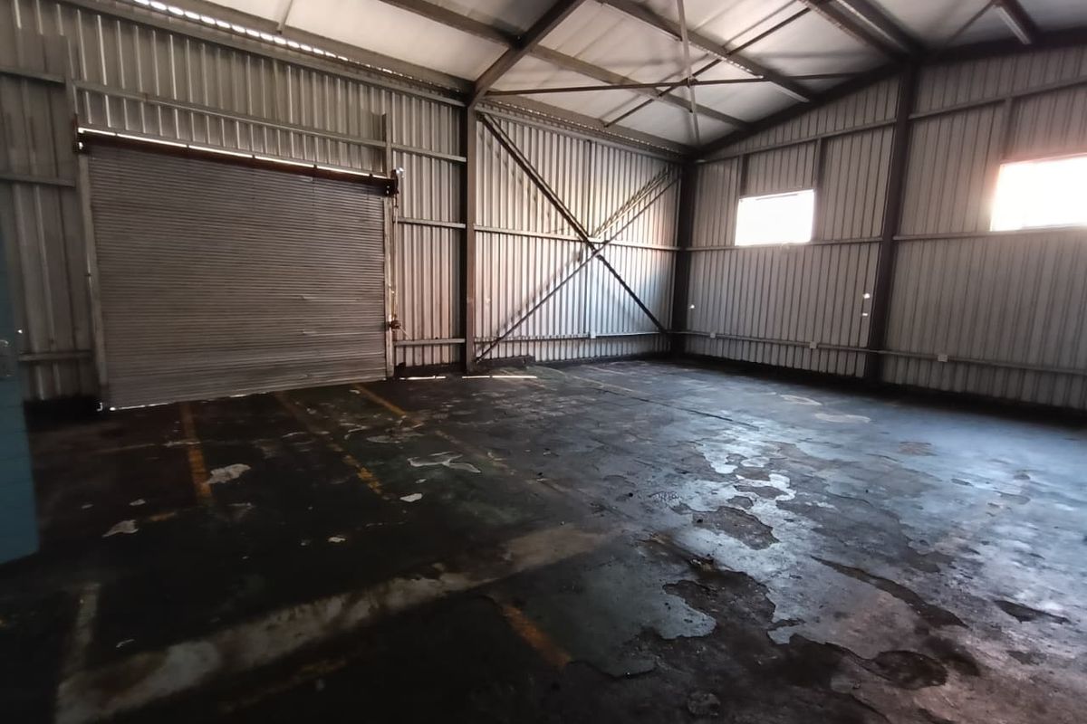 Spacious industrial warehouse or garage unit featuring high ceilings, exposed steel structural elements, and a large roller shutter door for vehicle or equipment access.