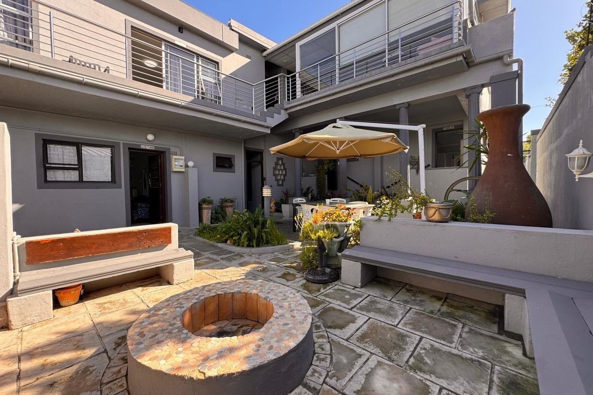 A spacious rear courtyard featuring a built-in fire pit, stone paving, and integrated bench seating, providing a functional outdoor entertainment area for guests.