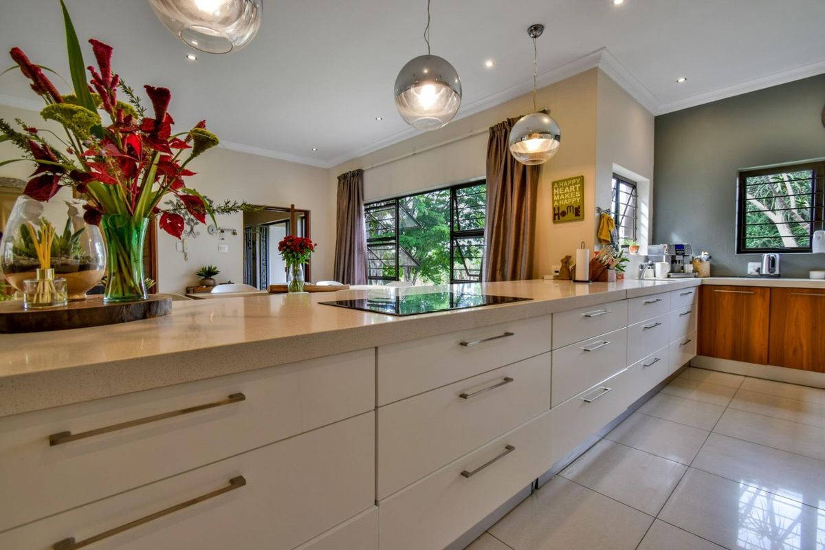 Modern kitchen featuring a long island with a built-in induction cooktop, sleek white cabinetry, stone countertops, and contemporary pendant lighting.