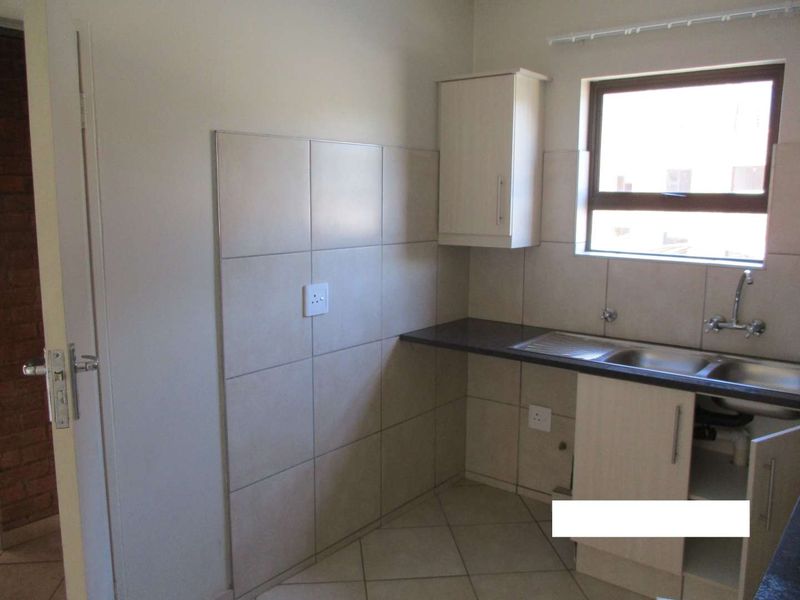 A compact kitchen area featuring tiled splashbacks, built-in cabinetry, and a stainless steel sink, offering a functional space ready for updates.