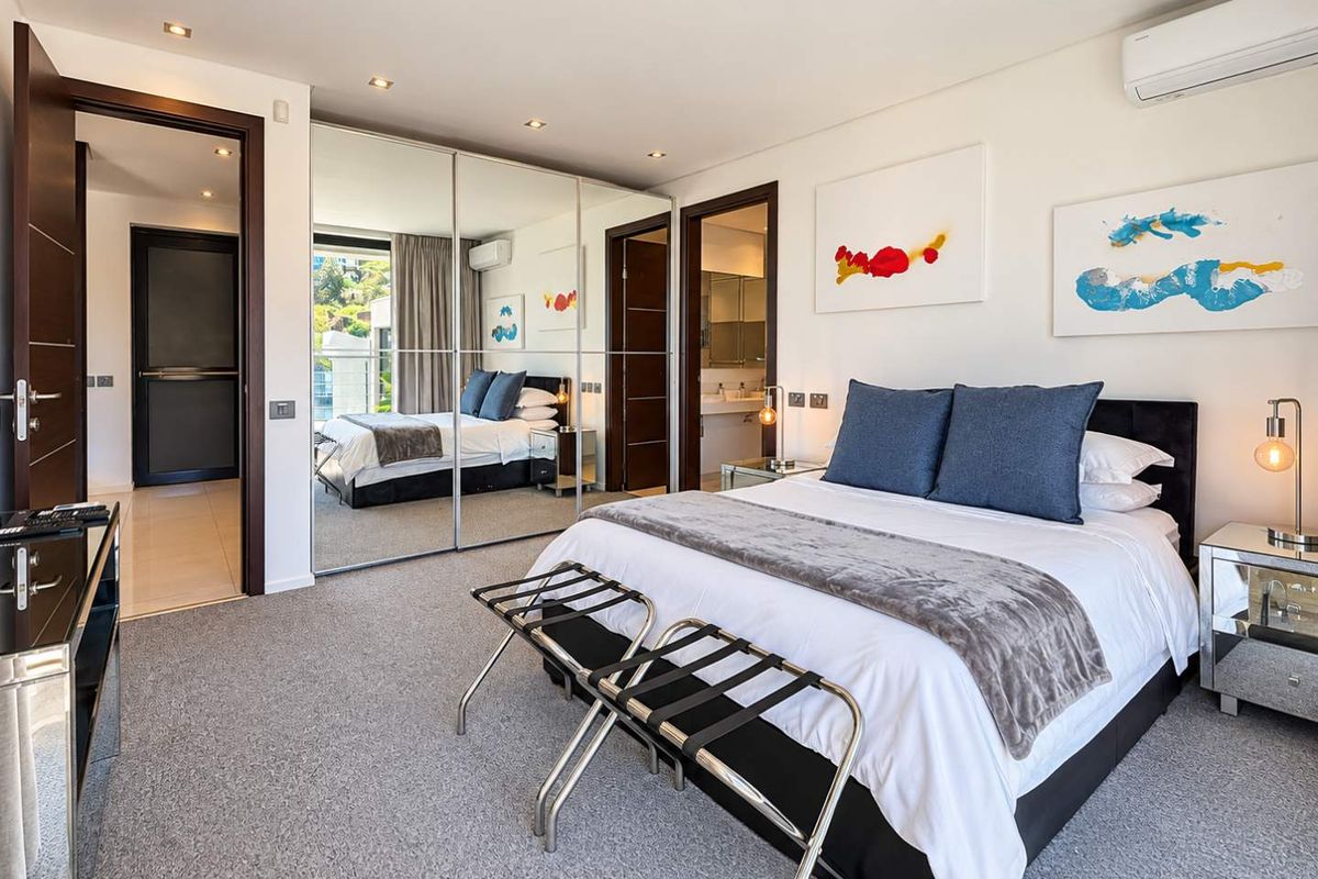 Modern bedroom featuring plush carpeting, mirrored built-in wardrobes, recessed lighting, and a wall-mounted air conditioning unit, with direct access to an en-suite bathroom.