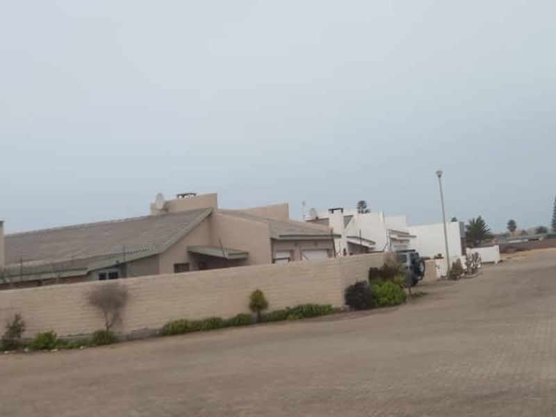 A street view showing the exterior of residential properties with paved roads, boundary walls, and tiled roofing under an overcast sky.