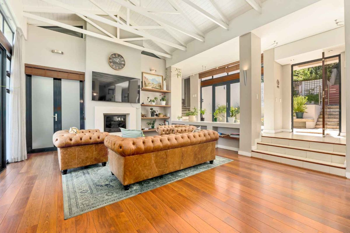 Spacious living room featuring vaulted ceilings with exposed beams, hardwood flooring, a built-in fireplace, and seamless access to an outdoor patio area.
