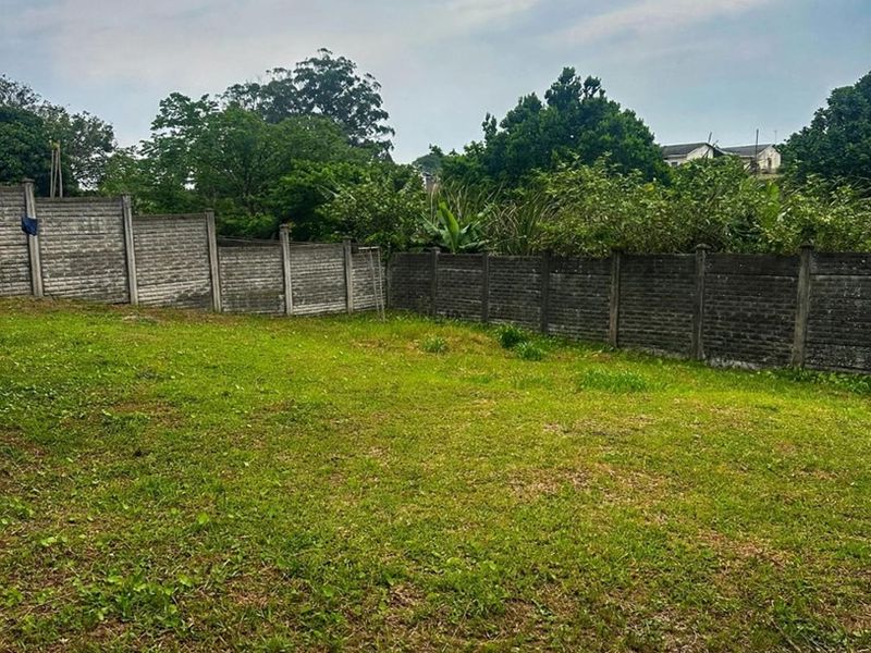 A spacious, level backyard area enclosed by precast concrete boundary walls, featuring established lawn and surrounding greenery.