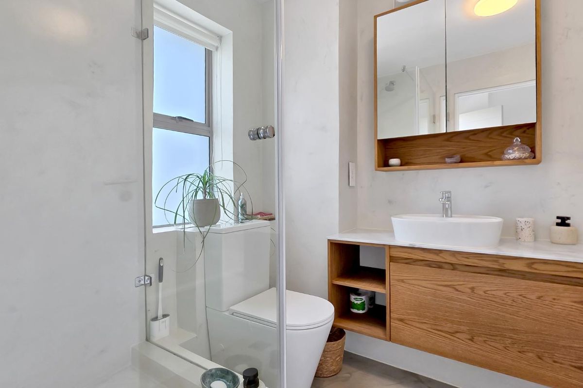 Modern bathroom featuring a timber vanity with vessel sink, mirrored cabinet, and a glass-enclosed shower area with clean finishes.