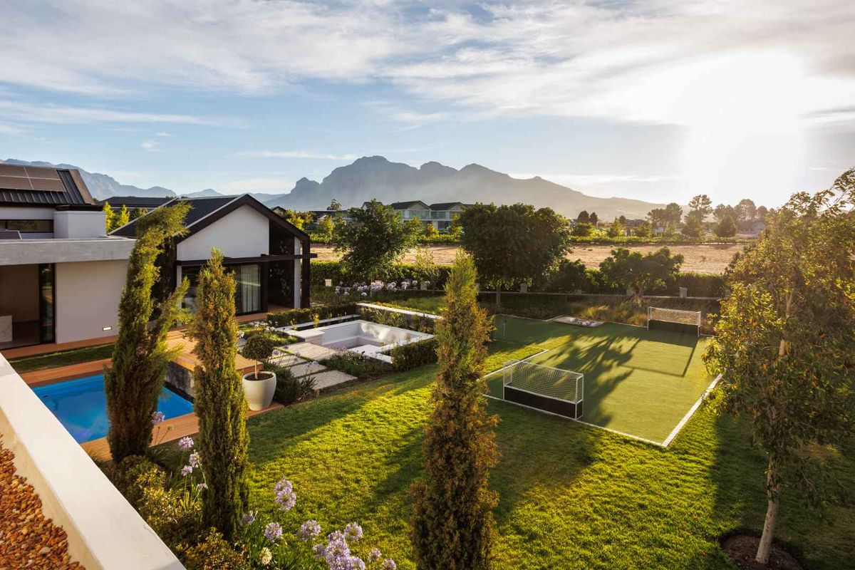 A beautifully landscaped rear garden featuring a swimming pool, sunken seating area, and a private sports field with mountain views.