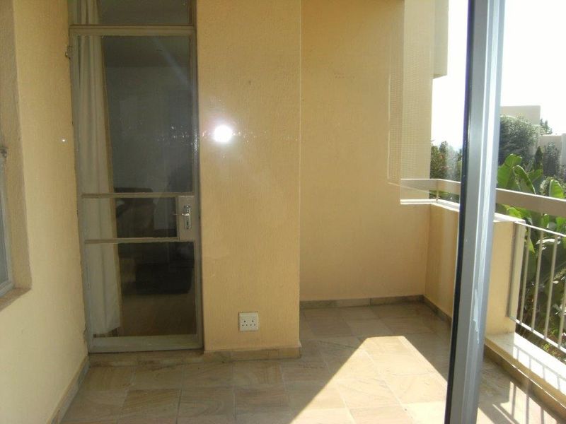 A covered balcony featuring tiled flooring, a metal balustrade, and a secure access door leading into the apartment interior.