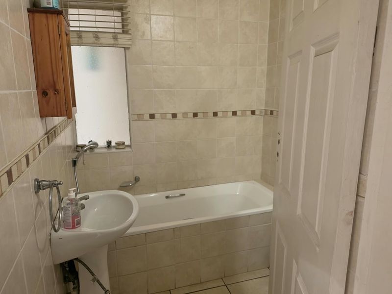 A functional bathroom featuring a pedestal basin, bathtub, and neutral wall tiling. The space is well-lit and ready for modern updates.