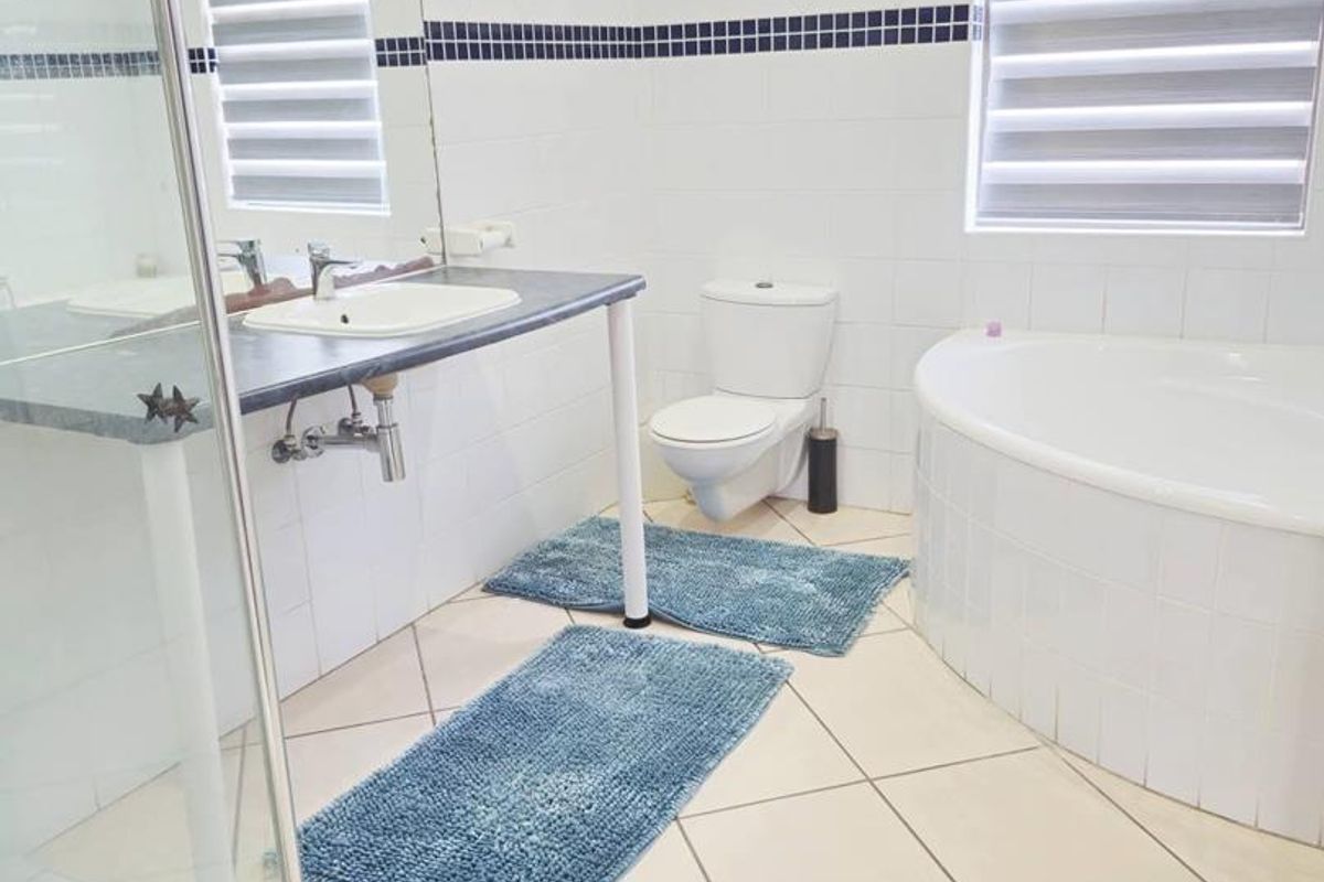 A functional bathroom featuring a corner bathtub, a separate glass-enclosed shower, a wall-mounted toilet, and a vanity basin with tiled flooring.
