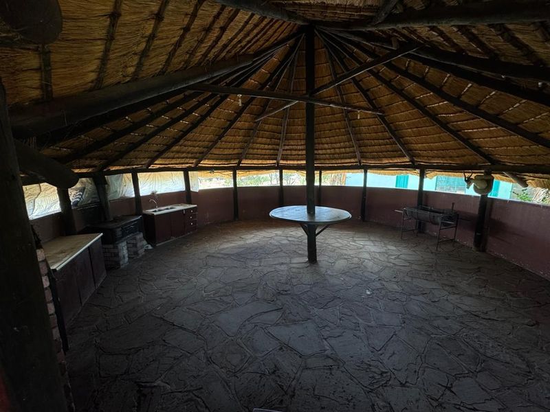 An open-air thatched lapa featuring stone flooring, built-in cabinetry with a sink, and a built-in braai area, ideal for outdoor entertaining.