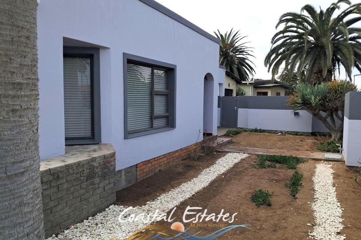 A view of the rear exterior of the house featuring a painted facade, aluminium window frames, and a landscaped garden area with a paved path.