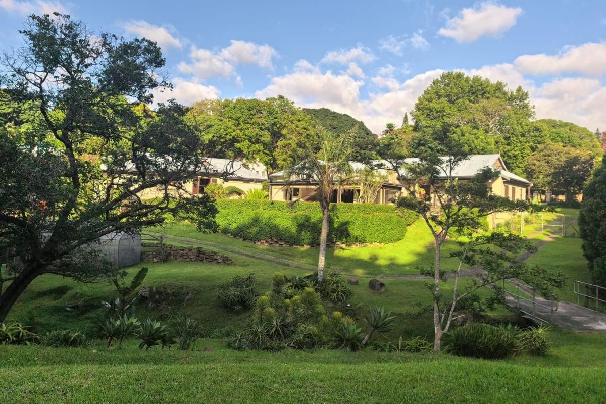 A scenic view of the rear elevation of the house, featuring a well-maintained garden, mature trees, and a small pedestrian bridge over a landscaped area.