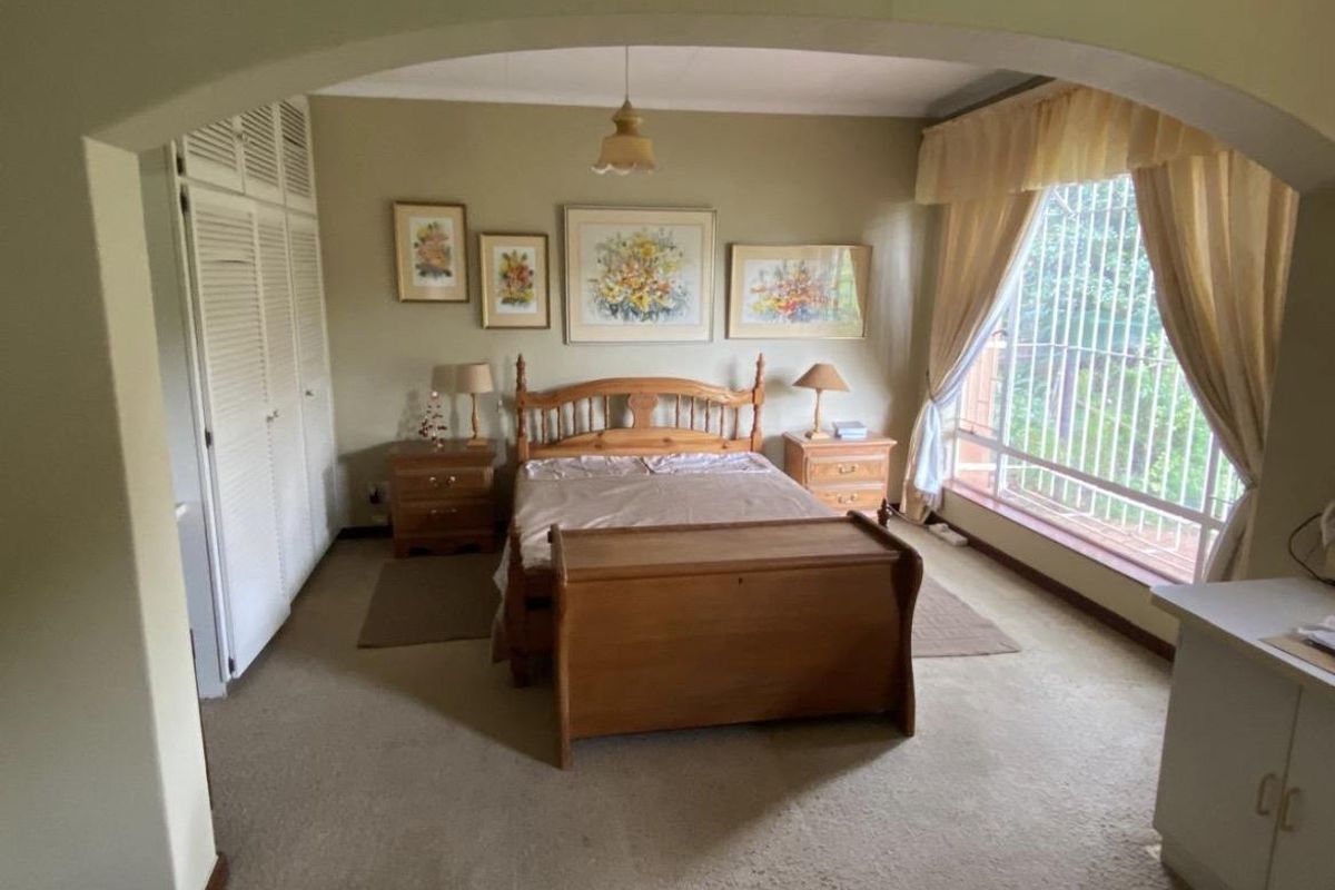 A spacious bedroom featuring built-in louvered closets, large windows with security bars, and an arched entryway, offering a comfortable and functional living space.