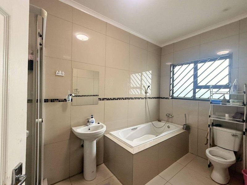 A functional bathroom featuring a pedestal basin, built-in bathtub, separate shower enclosure, and tiled finishes throughout.