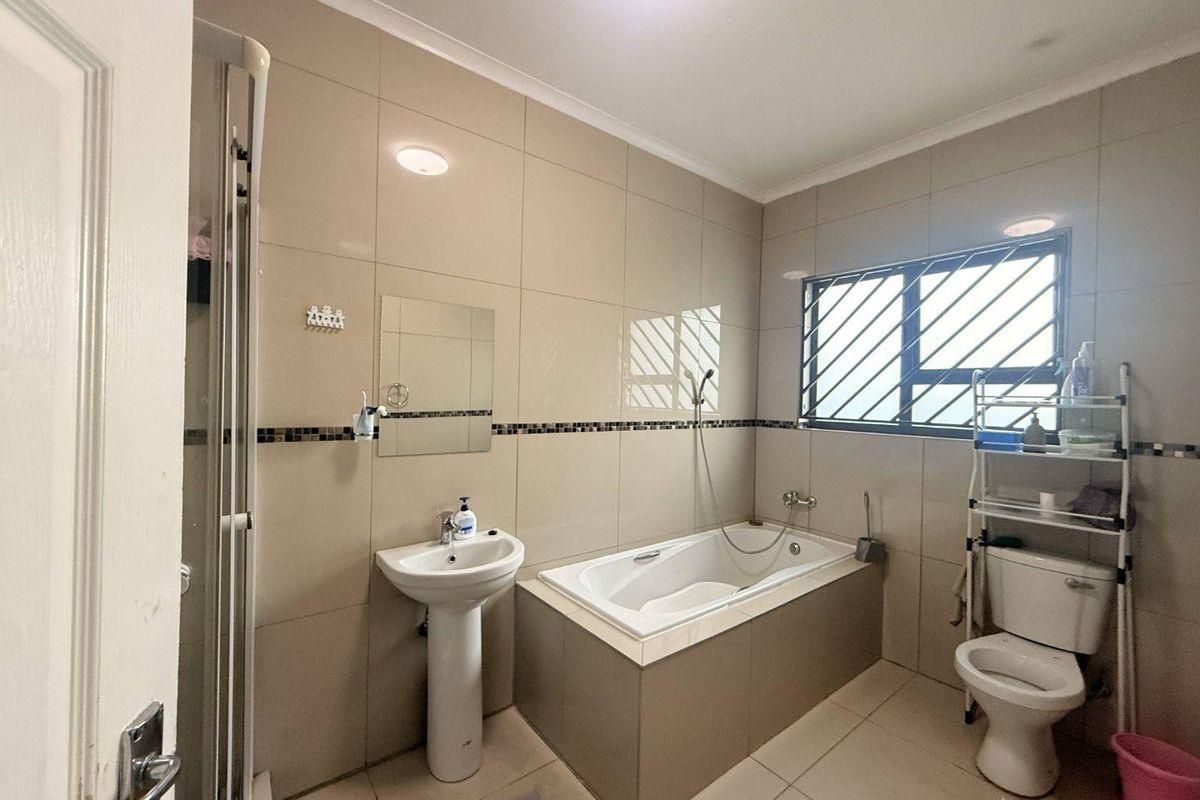 A functional bathroom featuring a pedestal basin, built-in bathtub, separate shower enclosure, and tiled finishes throughout.