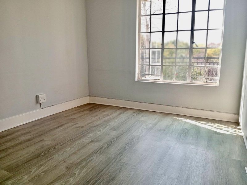 An empty bedroom featuring light-toned laminate flooring, a grid-pattern window, and neutral wall finishes, ready for personalization.