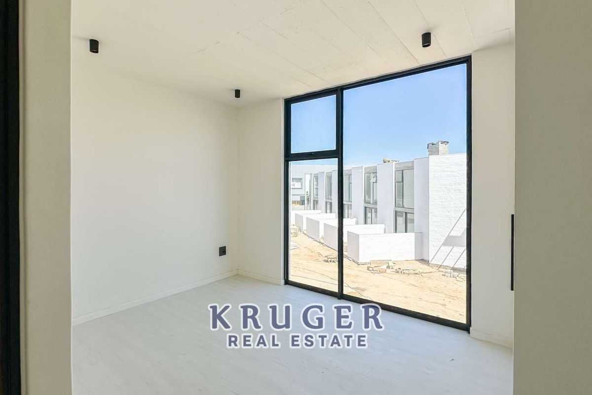 A bright, modern bedroom featuring floor-to-ceiling windows with views of the surrounding townhouse development.