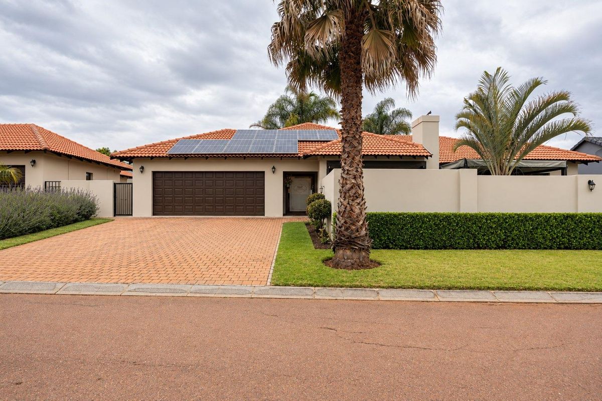 Well-maintained front elevation featuring a paved driveway, double garage, and roof-mounted solar panels, set behind a neat boundary wall and landscaped garden.