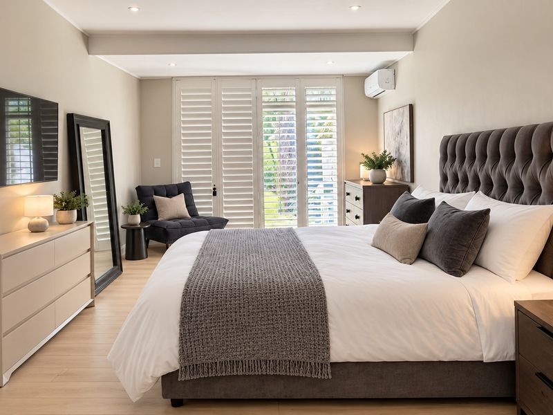 A well-appointed bedroom featuring light laminate flooring, plantation shutters, and a wall-mounted air conditioning unit, creating a bright and comfortable living space.