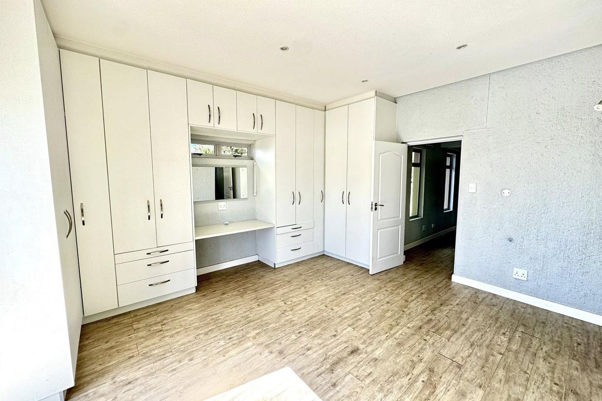 A spacious bedroom featuring extensive built-in white cabinetry with an integrated vanity desk, recessed ceiling lighting, and wood-look laminate flooring.