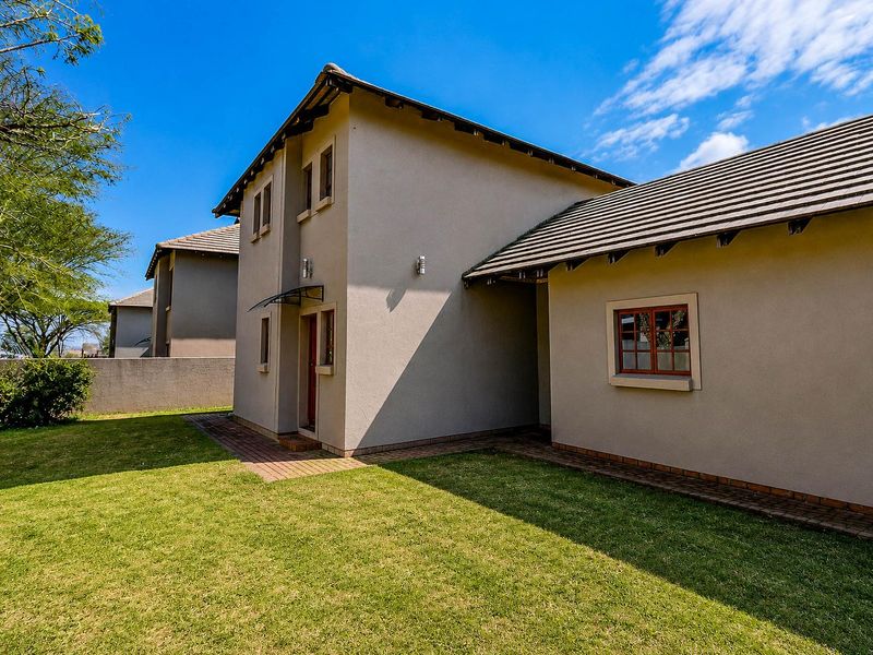 Rear view of the property featuring a well-maintained lawn, brick paved pathways, and a tiled roof structure.
