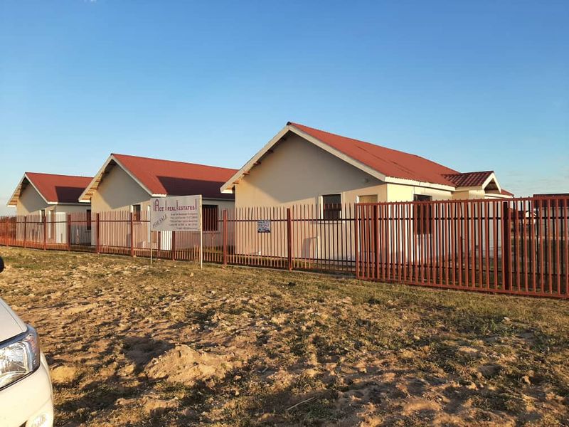 A row of newly constructed residential houses featuring pitched roofs and secured by metal palisade fencing.