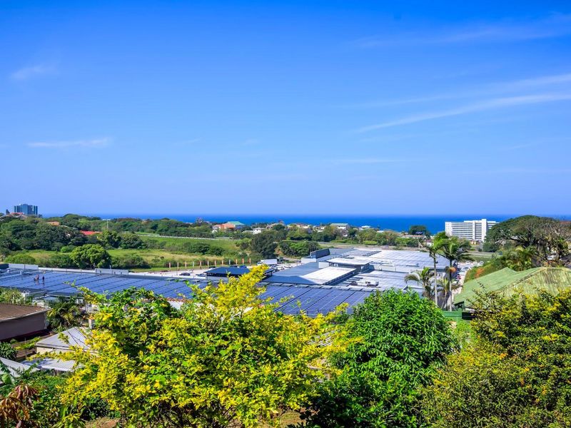 Elevated coastal view overlooking surrounding neighborhood, commercial buildings with solar panel installations, and the distant ocean horizon.