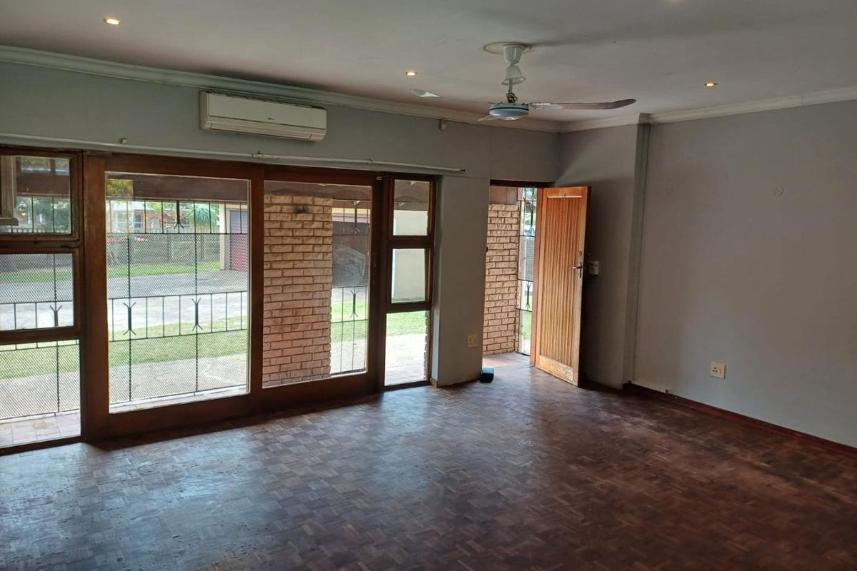 Spacious living area featuring classic parquet flooring, exposed brick accents, split-system air conditioning, and large timber-framed sliding doors providing access to the exterior.