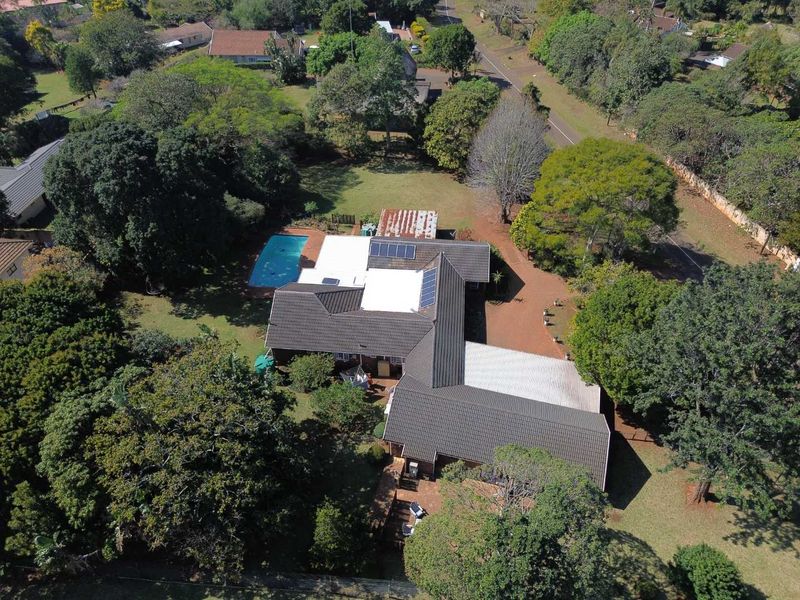 Aerial view of a residential property featuring a large garden, swimming pool, solar panels, and a multi-section tiled roof structure.