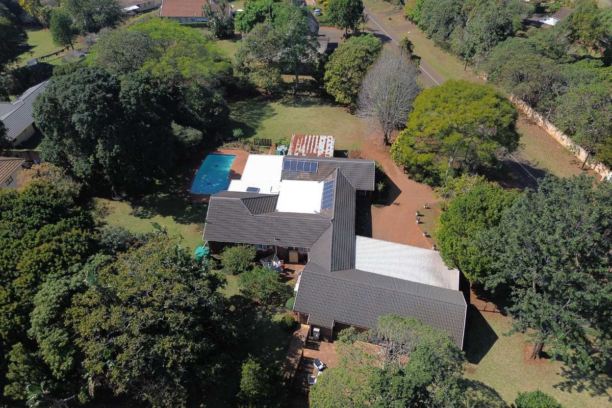 Aerial view of a residential property featuring a large garden, swimming pool, solar panels, and a multi-section tiled roof structure.