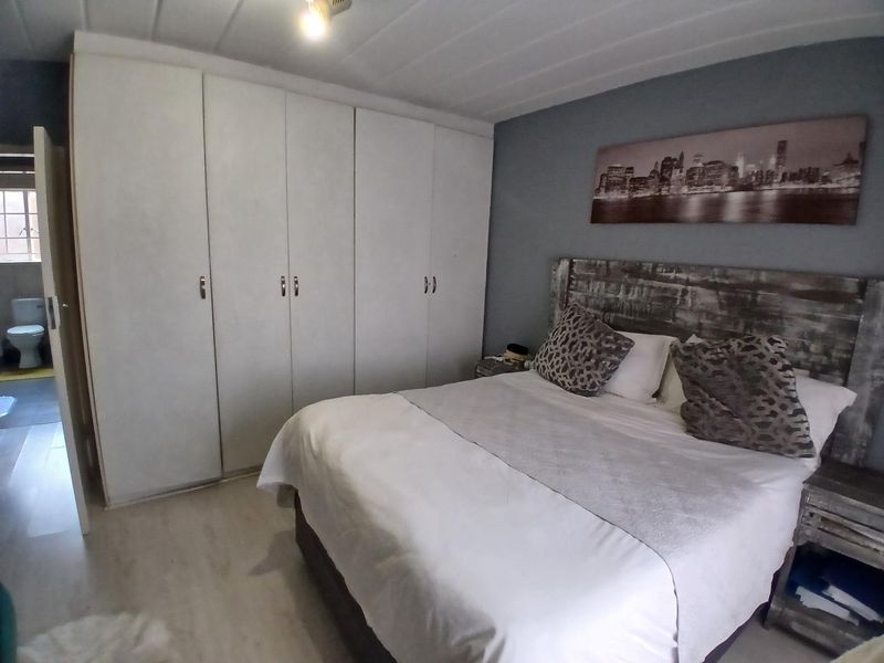 A bedroom featuring built-in cupboards, laminate flooring, and an adjoining bathroom view.
