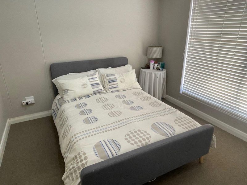 A functional bedroom featuring neutral wall tones, carpeted flooring, and venetian blinds for adjustable natural light control.